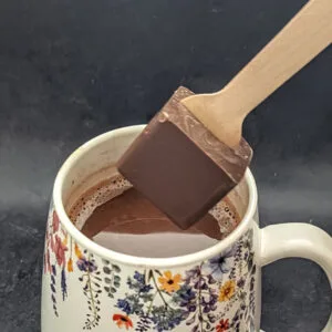 Artisan chocolate stirrer being dipped into hot milk by Chocolates by Design.