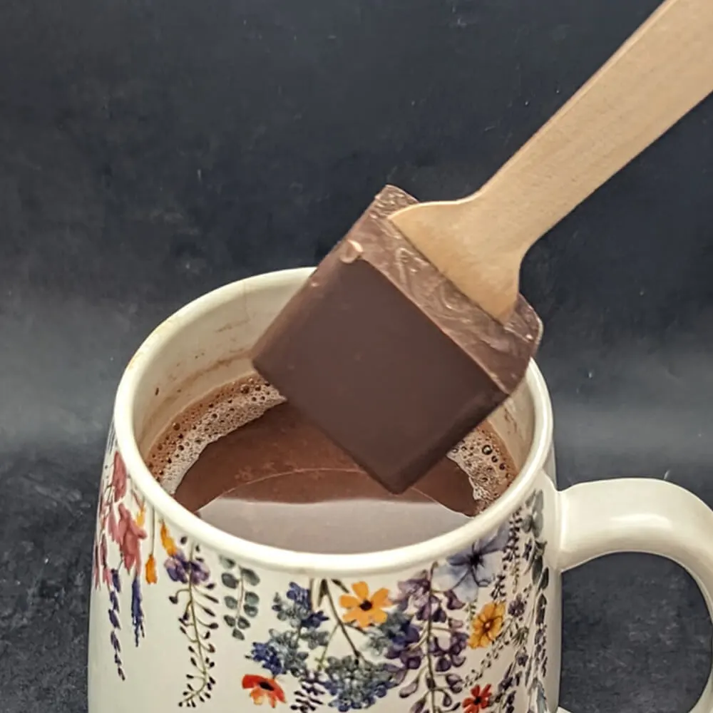 Artisan chocolate stirrer being dipped into hot milk by Chocolates by Design.